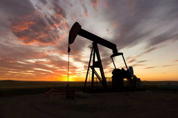 Silhouette of an oil pumpjack against a colorful sunset sky, with orange and purple clouds stretching over a flat landscape.