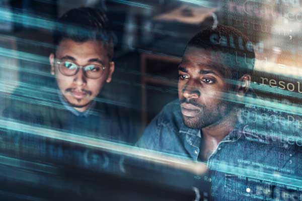 Two men focused on a computer screen, with lines of code superimposed over the image, suggesting they are working on programming or software development.